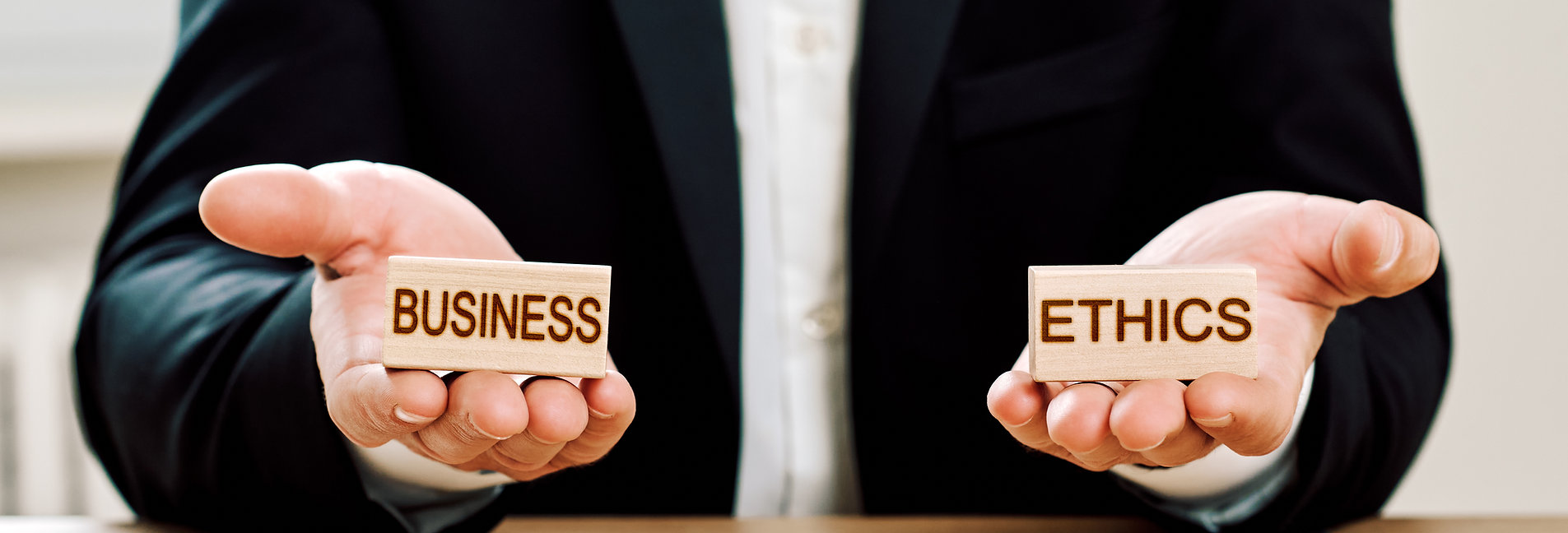 Two hands holding wooden blocks reading 'BUSINESS' and 'ETHICS'